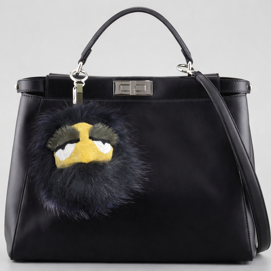 Black handbag with a Fendi fur monster charm clipped to the bag.
