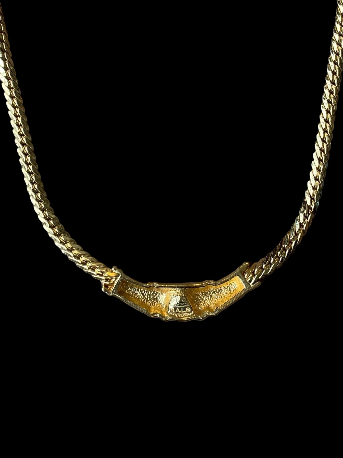A close view of the back Swarovski Gold Necklace with Black Crystal Centre on the black fabric background. SAL initials shown.