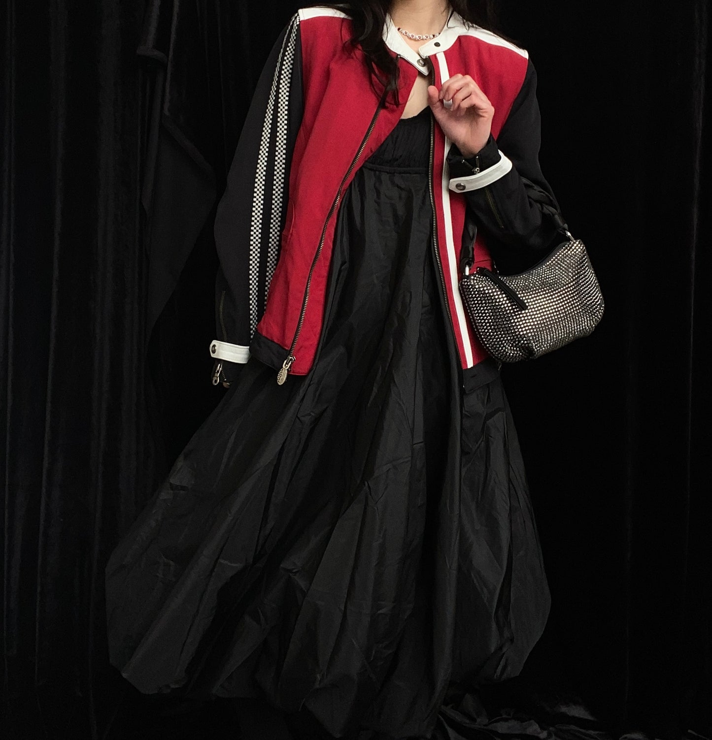 Person wearing a red and black jacket over the Isabel Toledo Sculptural Taffeta Dress, with a handbag on their arm, on black background.