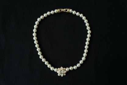 Swarovski Pearl Necklace with Geometric Crystal Centre. Set in gold-tone metal, sitting on a black fabric background.


