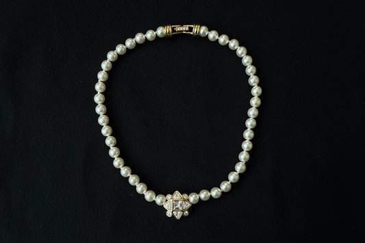 Swarovski Pearl Necklace with Geometric Crystal Centre. Set in gold-tone metal, sitting on a black fabric background.


