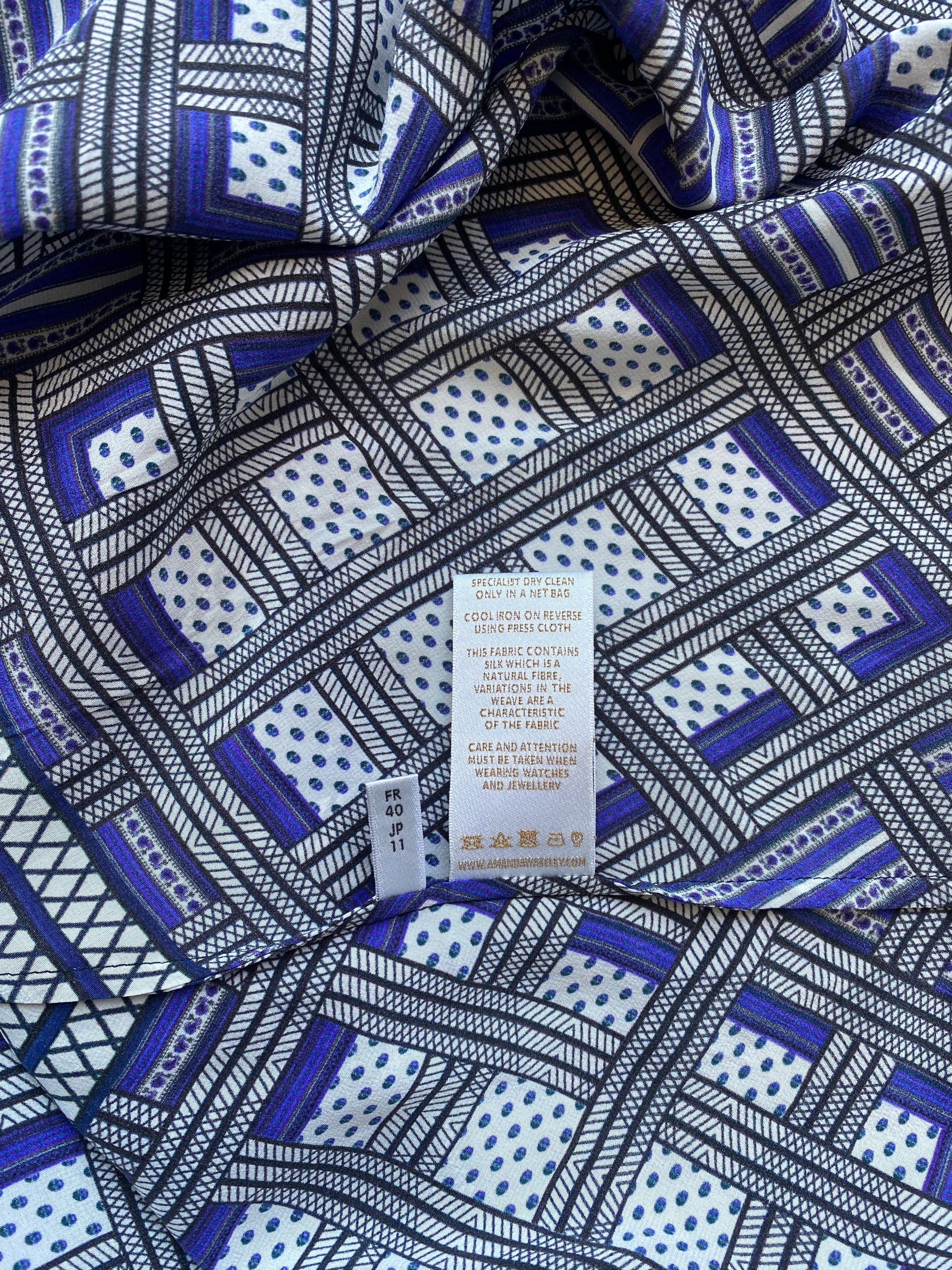 A close up image of the labels inside the Amanda Wakeley Silk Wrap Dress. Geometric print in shades of blue. 