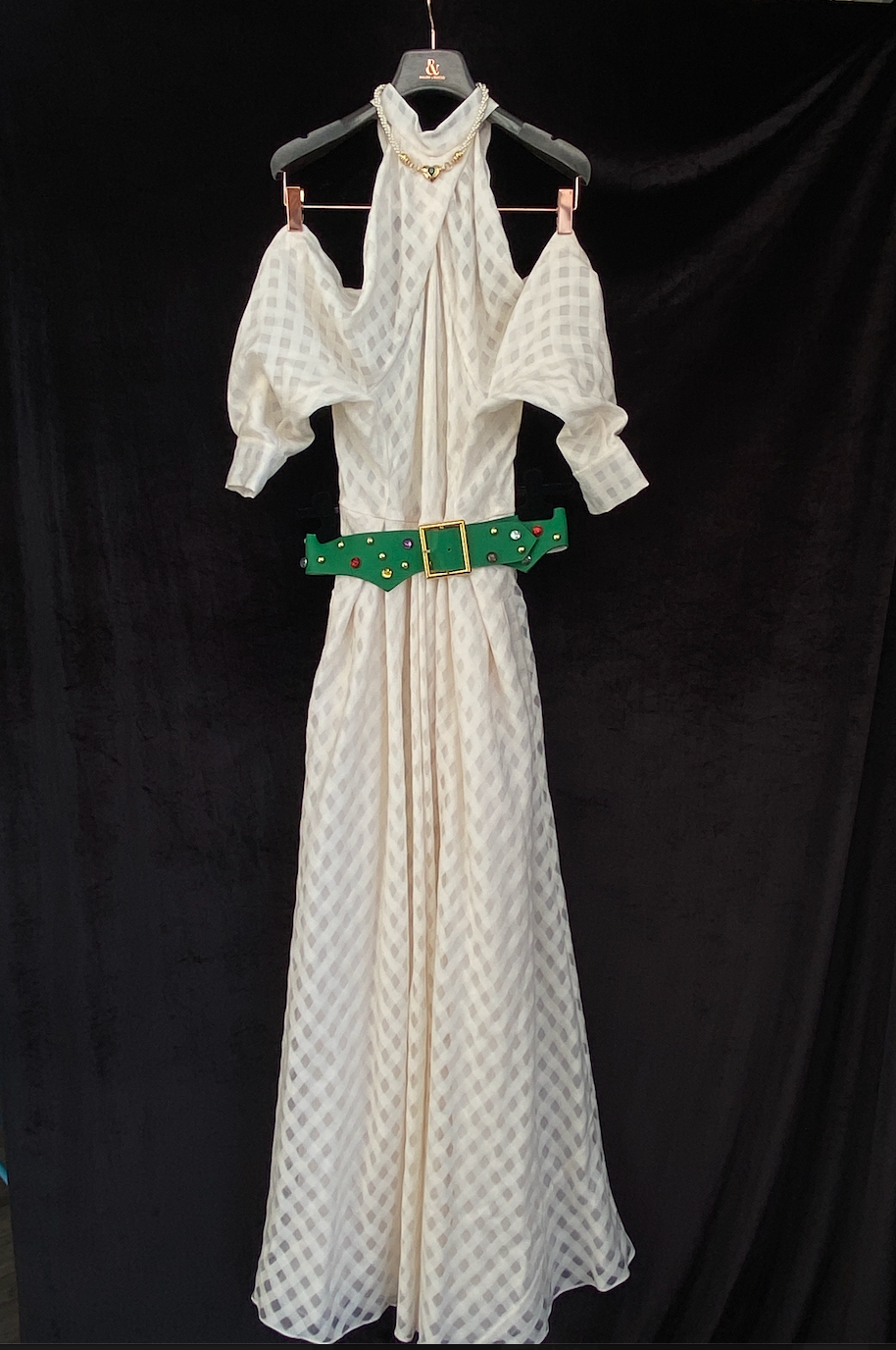 Ralph & Russo “Snow White” Cut-Out Dress with a green belt, hanging on a hanger, on a black background.