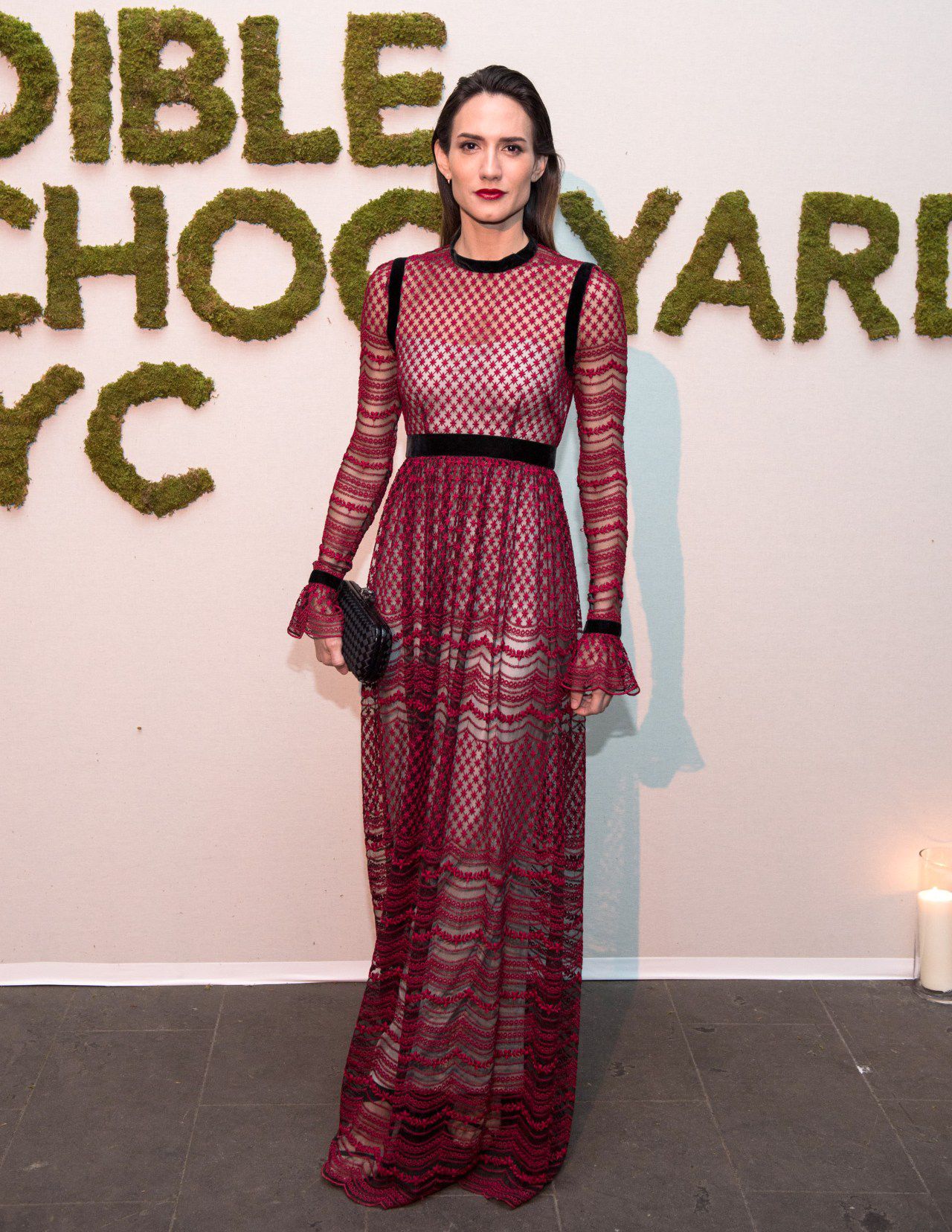 Woman modelling a Philosophy di Lorenzo Seraphini burgundy long sleeve gown dress against a white background with text on the wall.