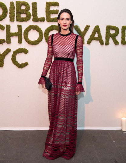 Woman modelling a Philosophy di Lorenzo Seraphini burgundy long sleeve gown dress against a white background with text on the wall.