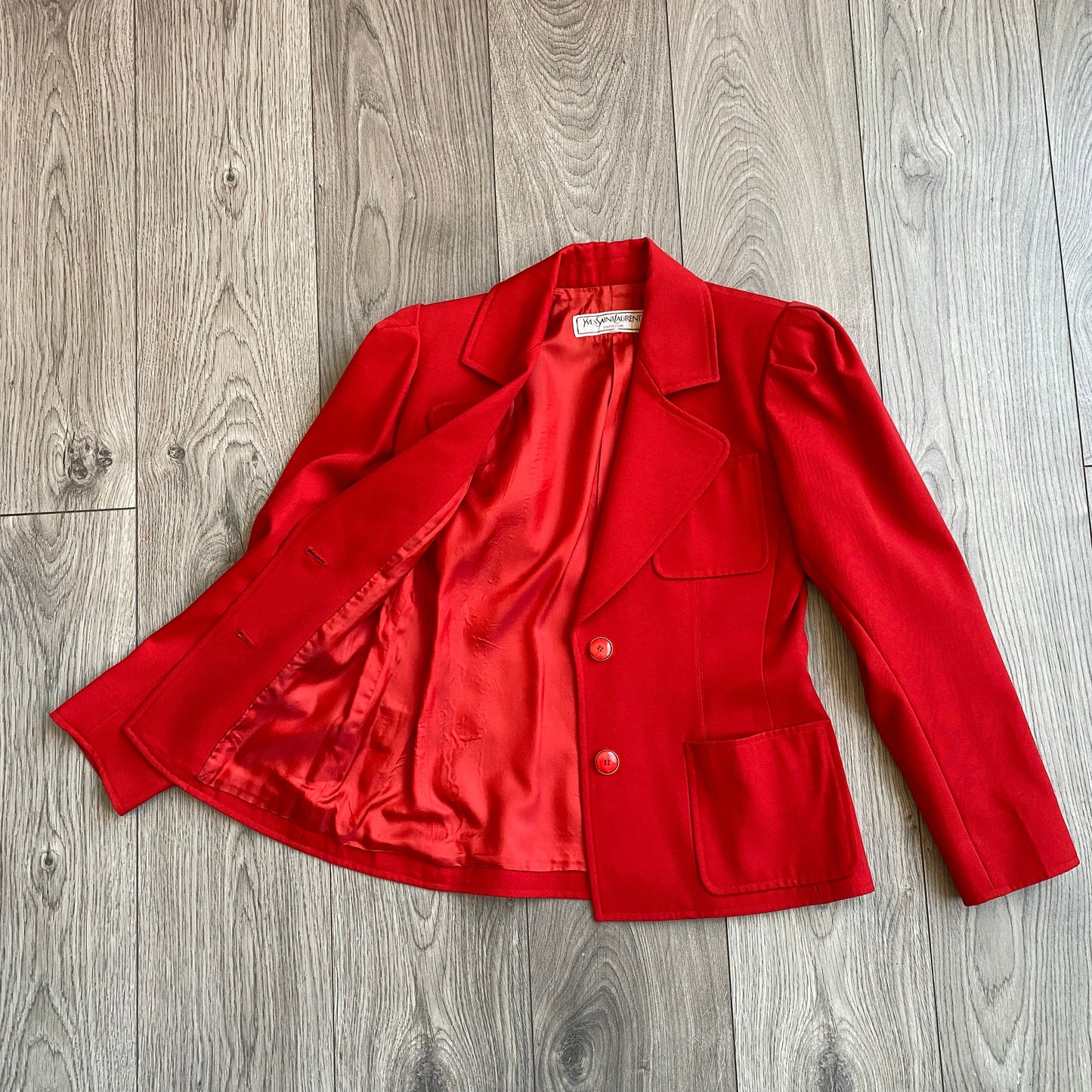 Vibrant red Yves Saint Laurent Rive Gauche Variation Jacket, laid on a wooden floor with one side open revealing the red inside lining.