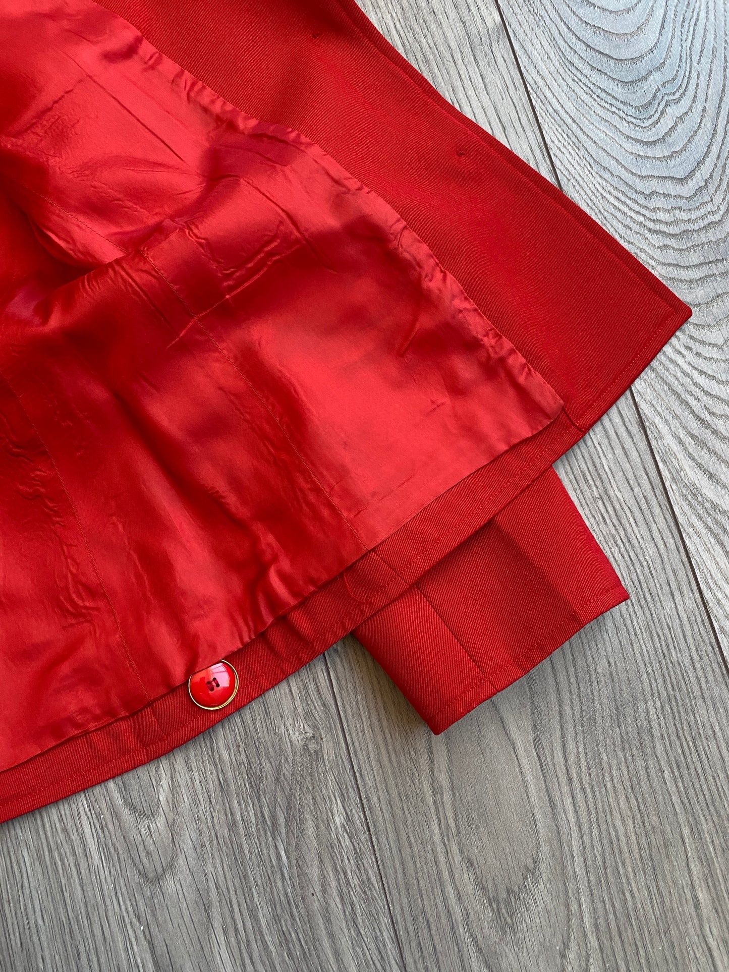 Close up view of the inside lining of the vibrant red Yves Saint Laurent Rive Gauche Variation Jacket, laid on a wooden floor.